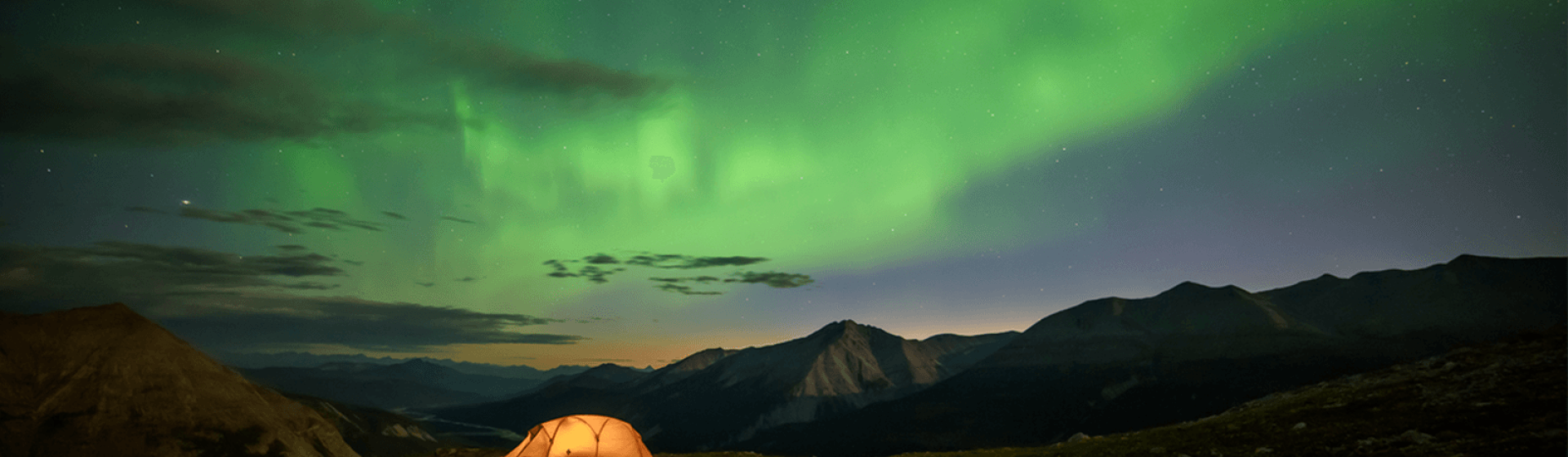 Orange, glowing tent against dark background with the Northern Lights in the sky above